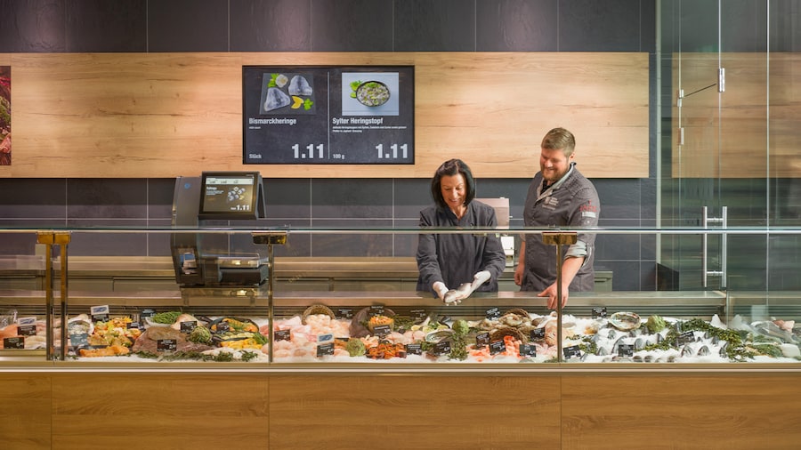 Zwei lächelnde Mitarbeitende legen Fisch in eine lange Bedientheke.